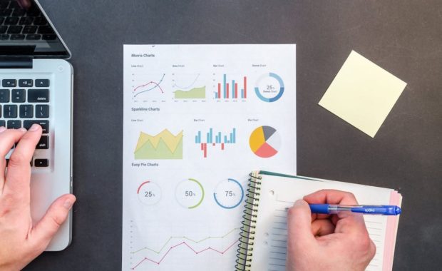 A person writing on a paper with graphs and charts.