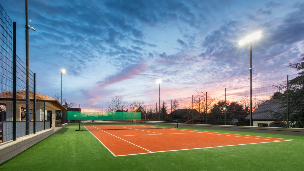 A tennis court with the sun setting in the background.