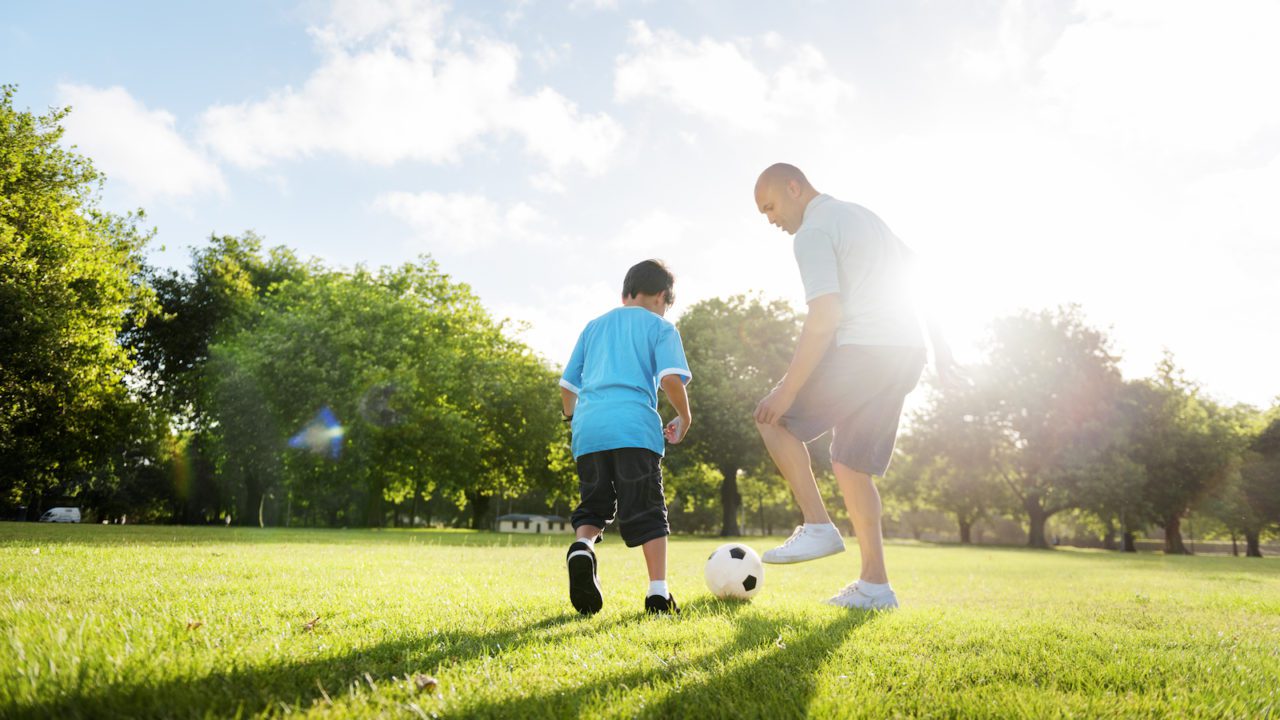 A man and boy playing soccer in the park.